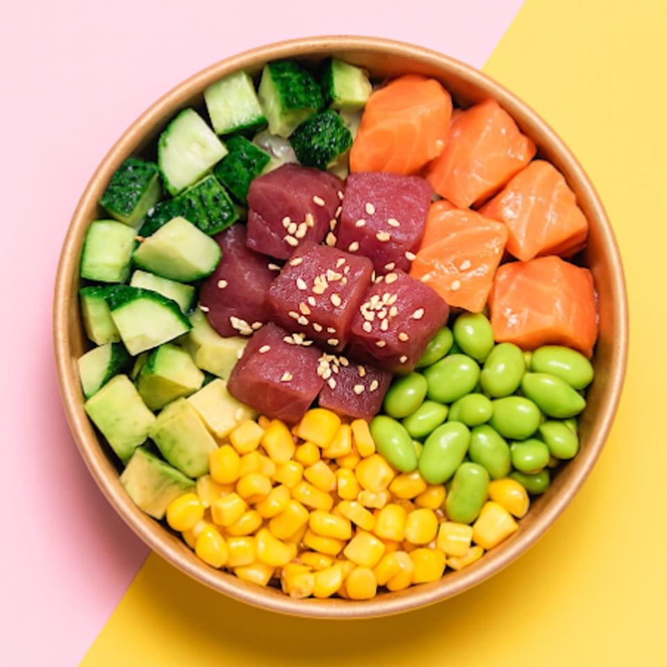A colorful poke bowl with tuna, salmon, cucumber, avocado, corn, and edamame.