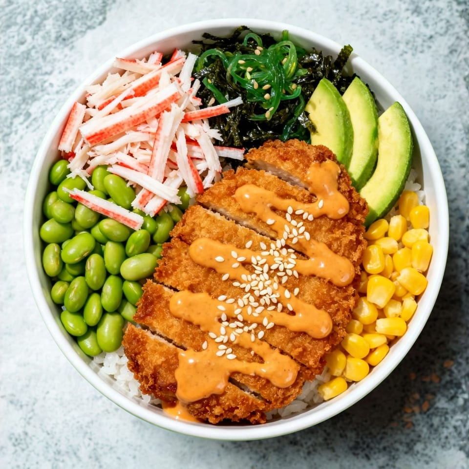A colorful sushi bowl with fried chicken, crab sticks, edamame, seaweed, corn, and avocado.