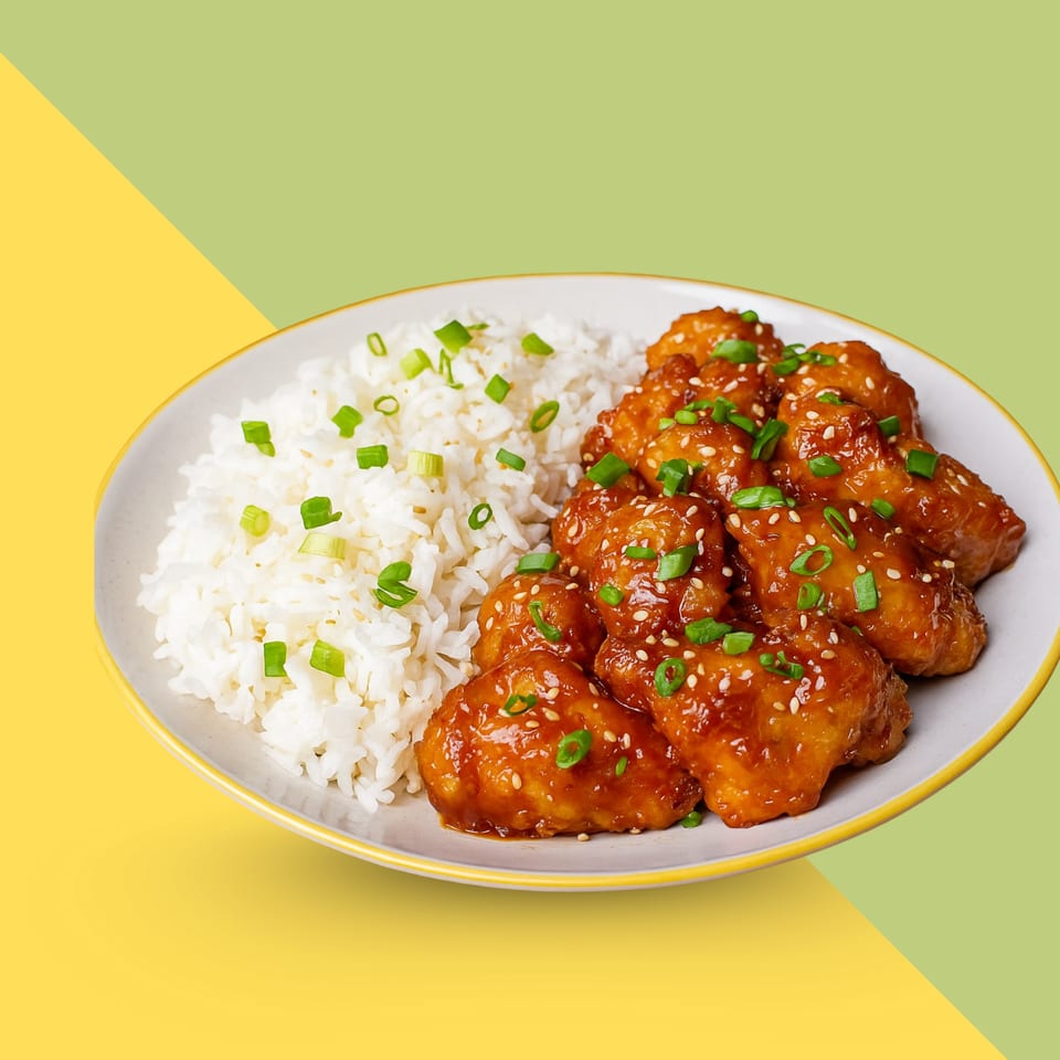 Sweet and sour chicken with white rice, garnished with sesame seeds and green onions.